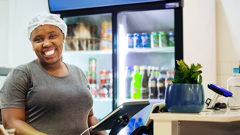 A smiling merchant working at a shop counter with a payment device
